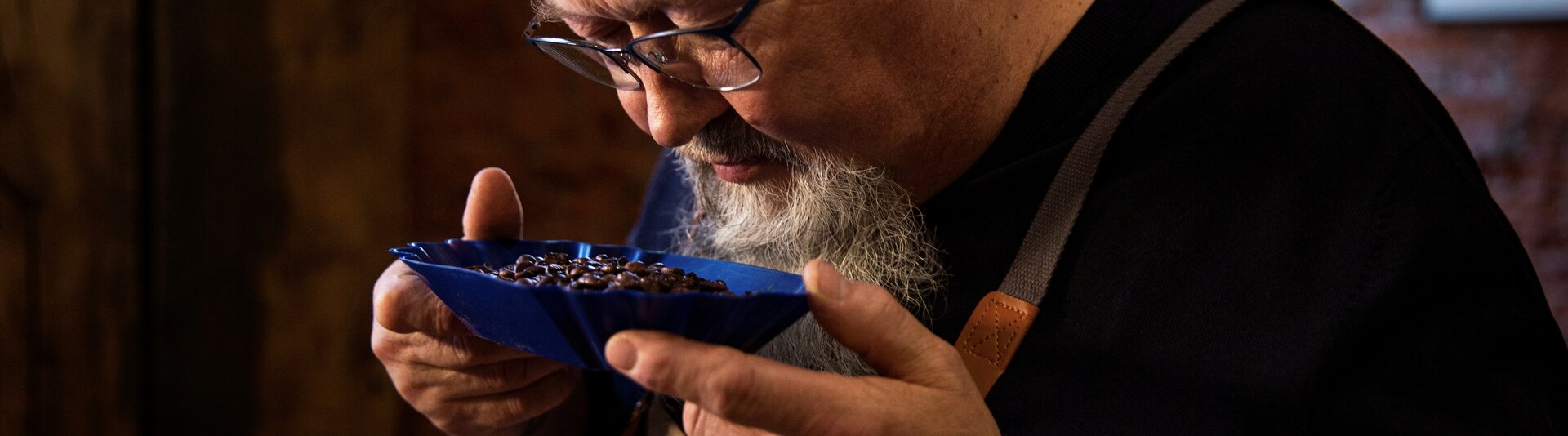 Freddy Bohnen riecht an Kaffeebohnen aus einer blauen Schale in einer rustikalen Umgebung und fängt die Kunst der Kaffeeverkostung ein.