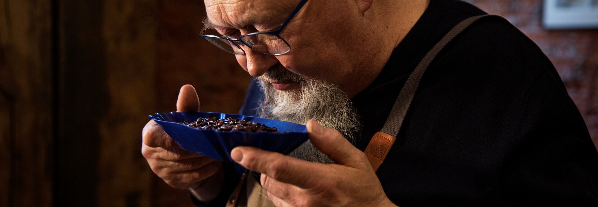 Freddy Bohnen riecht an Kaffeebohnen aus einer blauen Schale in einer rustikalen Umgebung und fängt die Kunst der Kaffeeverkostung ein.