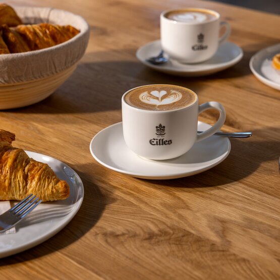 Leckere Croissants und Milchkaffee werden an einem Holztisch serviert, perfekt für ein charmantes Café-Erlebnis.