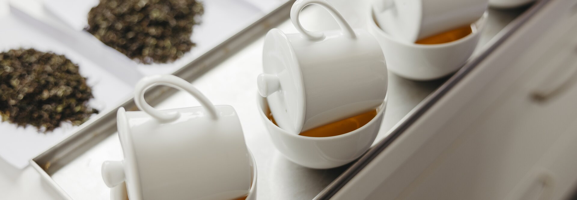 Auf einem Tablett werden Tassen mit aufgebrühtem Tee und Proben von losem Tee zur Verkostung bereitgestellt.