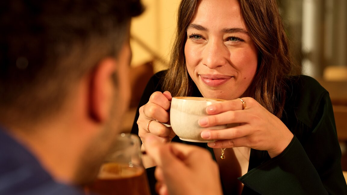 Zwei Freunde, die in einem warmen, einladenden Café einen Kaffee trinken, lächeln und sich unterhalten.