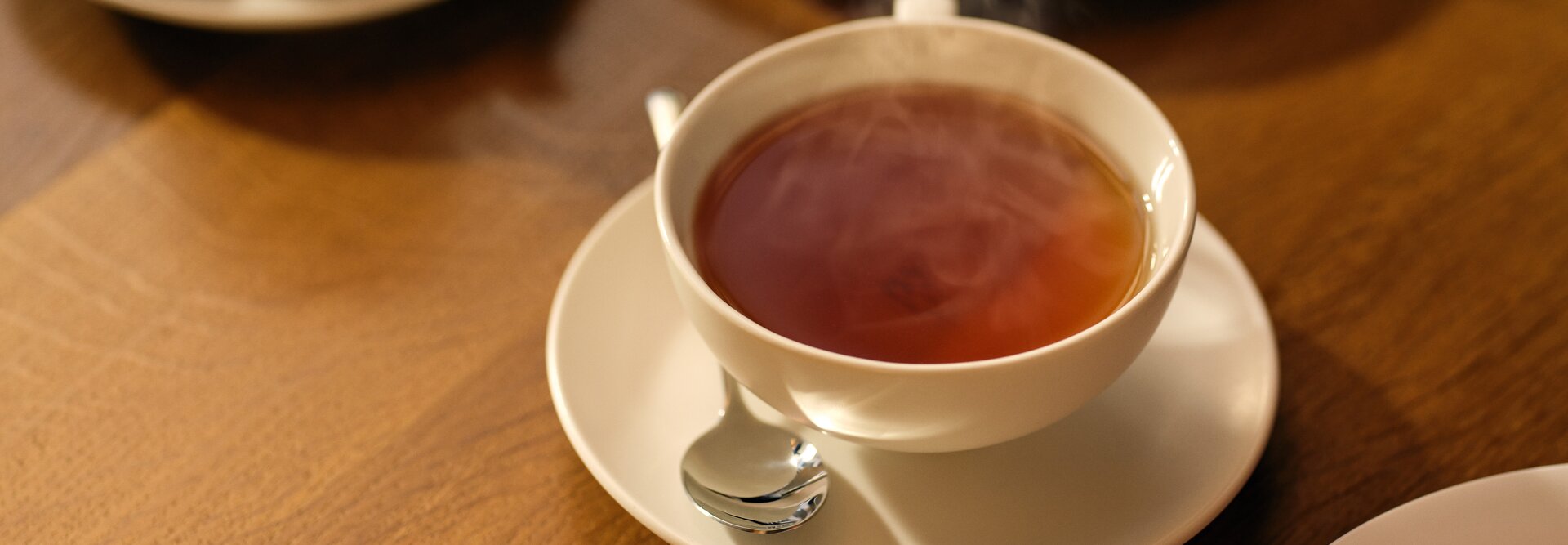 Eine dampfende Tasse Tee auf einem Holztisch, begleitet von köstlichen Desserts im Hintergrund.