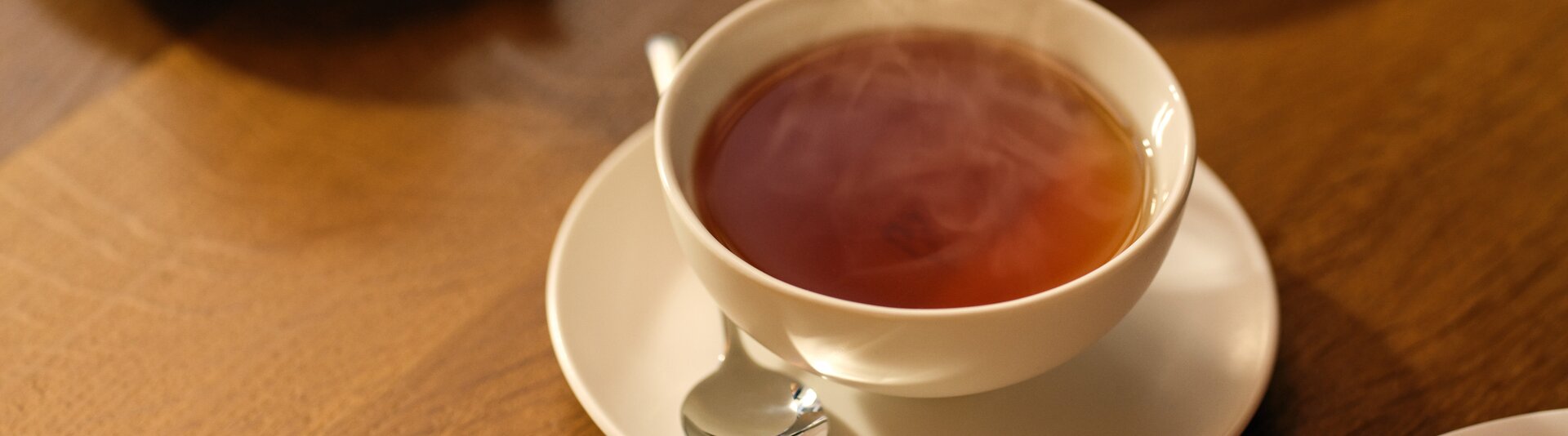 Eine dampfende Tasse Tee auf einem Holztisch, begleitet von köstlichen Desserts im Hintergrund.