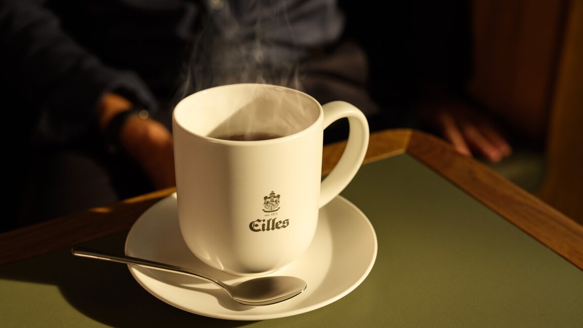 Eine dampfende Tasse Eilles-Kaffee auf einer Untertasse, aufgestellt auf einem stilvollen Tisch. Perfekt für Kaffee-Liebhaber.