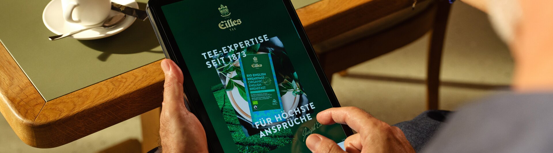Person enjoying tea and coffee while browsing Eilles Tea expertise on a tablet at a table.