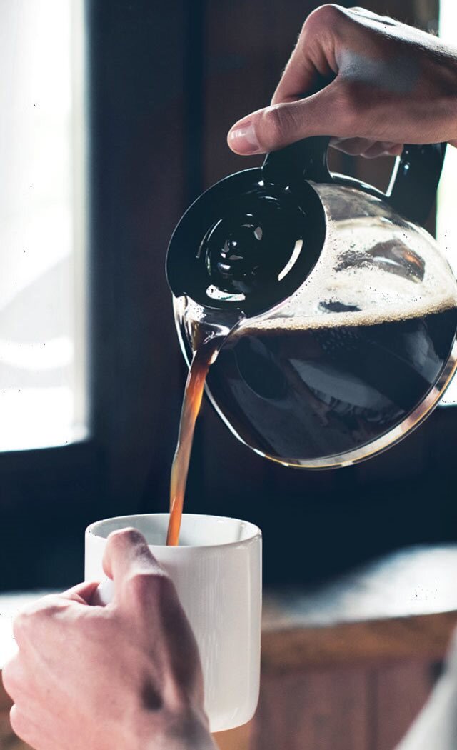 Frisch gebrühten Kaffee aus einer Filterkaffeemaschine in eine weiße Tasse gießen und damit einen warmen, gemütlichen Moment festhalten.