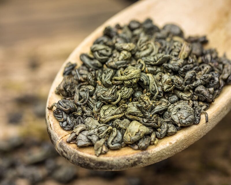 Lose Grünteeblätter, die auf einem Holzlöffel präsentiert werden und ihre einzigartige gewellte Textur und satte Farbe zur Geltung bringen.