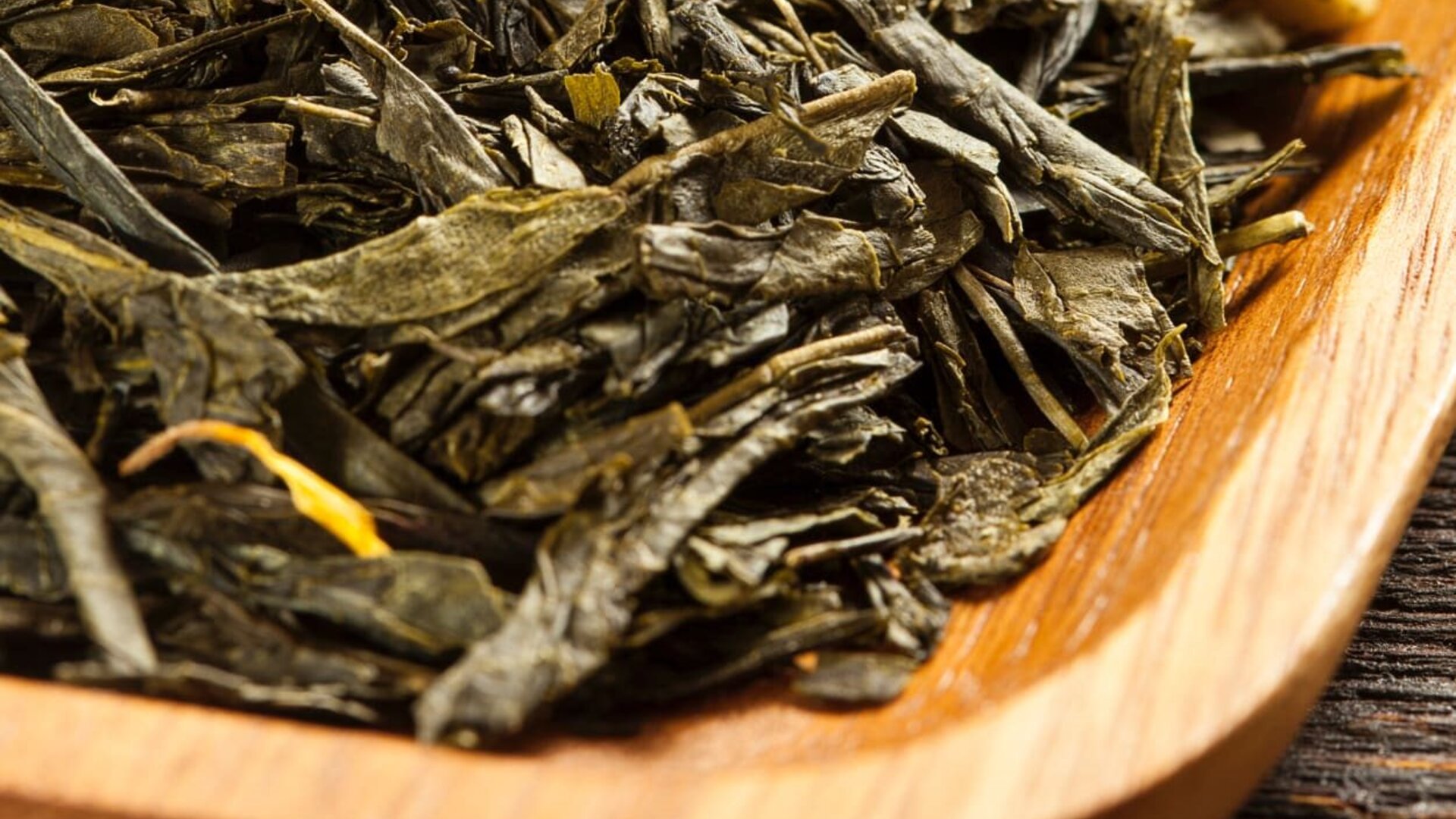 Lose Grünteeblätter in einer Holzschale, die ihre leuchtende Farbe und reiche Textur zur Geltung bringen. Perfekt für Teeliebhaber.