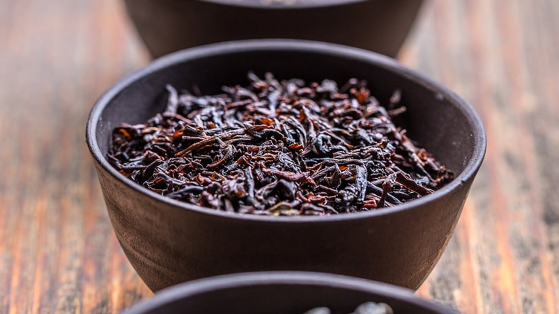 Lose Schwarzteeblätter in rustikalen Schalen, die ihre reiche Farbe und Textur auf einer hölzernen Oberfläche zur Geltung bringen.