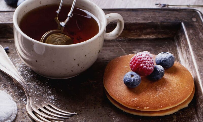 Warmer schwarzer Tee begleitet die Pfannkuchen mit frischen Beeren auf einem rustikalen Tablett, perfekt für ein köstliches Frühstück.