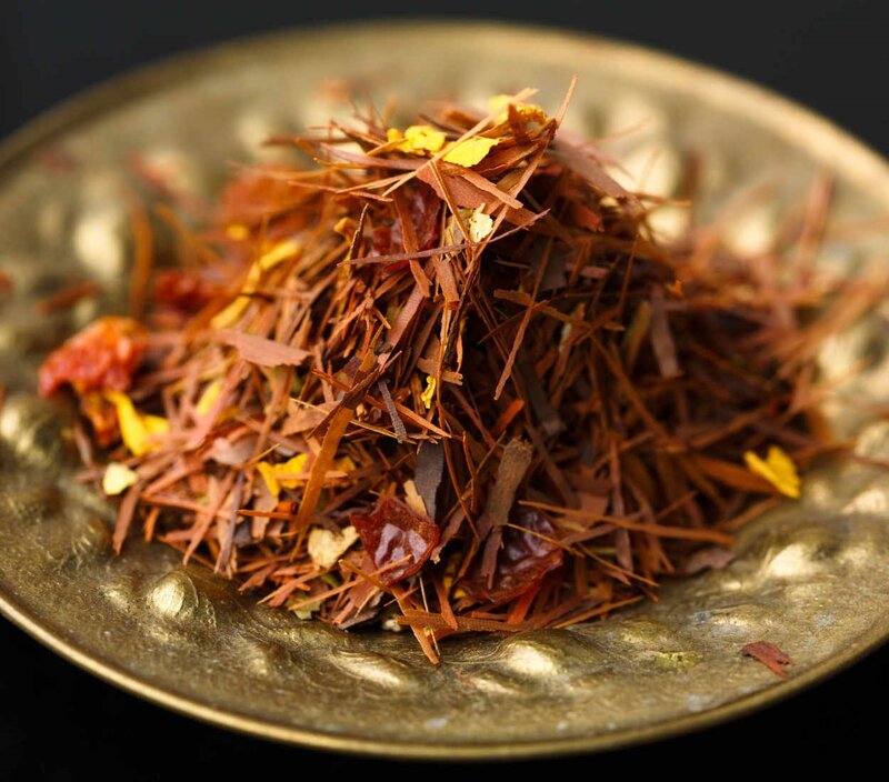 Rooibos-Teeblätter und Blütenblätter auf einem dekorativen Teller, der leuchtende Farben und Strukturen zeigt.