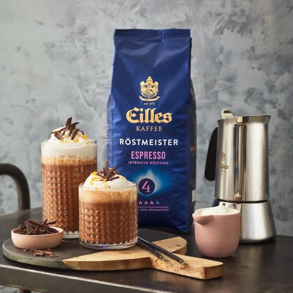 Eilles Röstmeister Espresso mit aufgeschlagenen Schokoladengetränken, garniert mit Schokoladenspänen auf einem Holztablett.