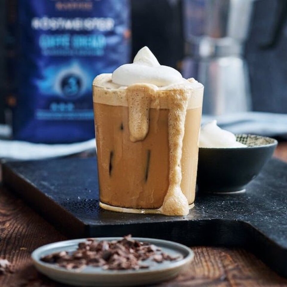 Gekühlter Vanille-Eiskaffee mit Schlagsahne, serviert mit Schokoladenspänen auf einer Holzunterlage.