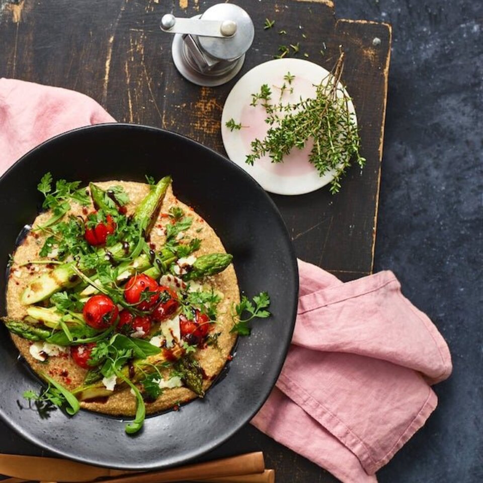 Leckere Polenta mit gegrilltem Spargel, Kirschtomaten und Kräutern, serviert auf einem rustikalen Holztisch.