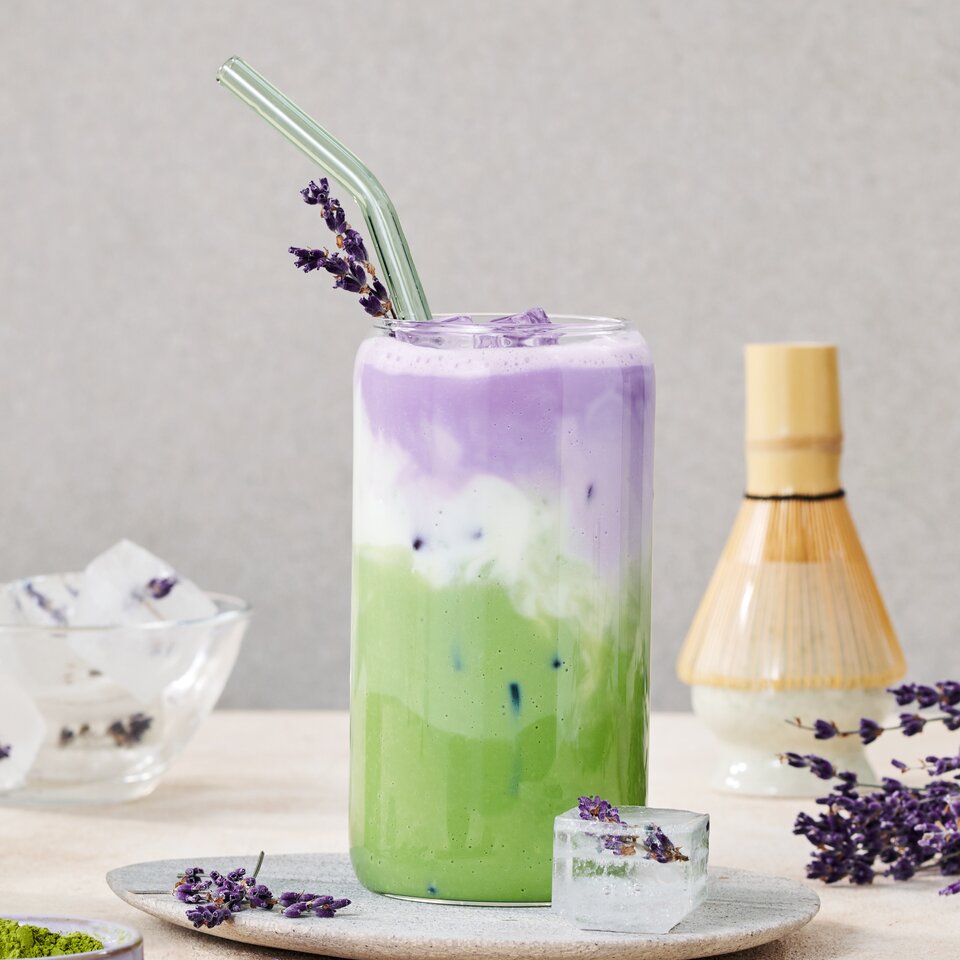 Geeister Lavendel-Matcha-Latte, garniert mit Lavendel, serviert in einem Glas mit Eiswürfeln und Matcha-Pulver an der Seite.