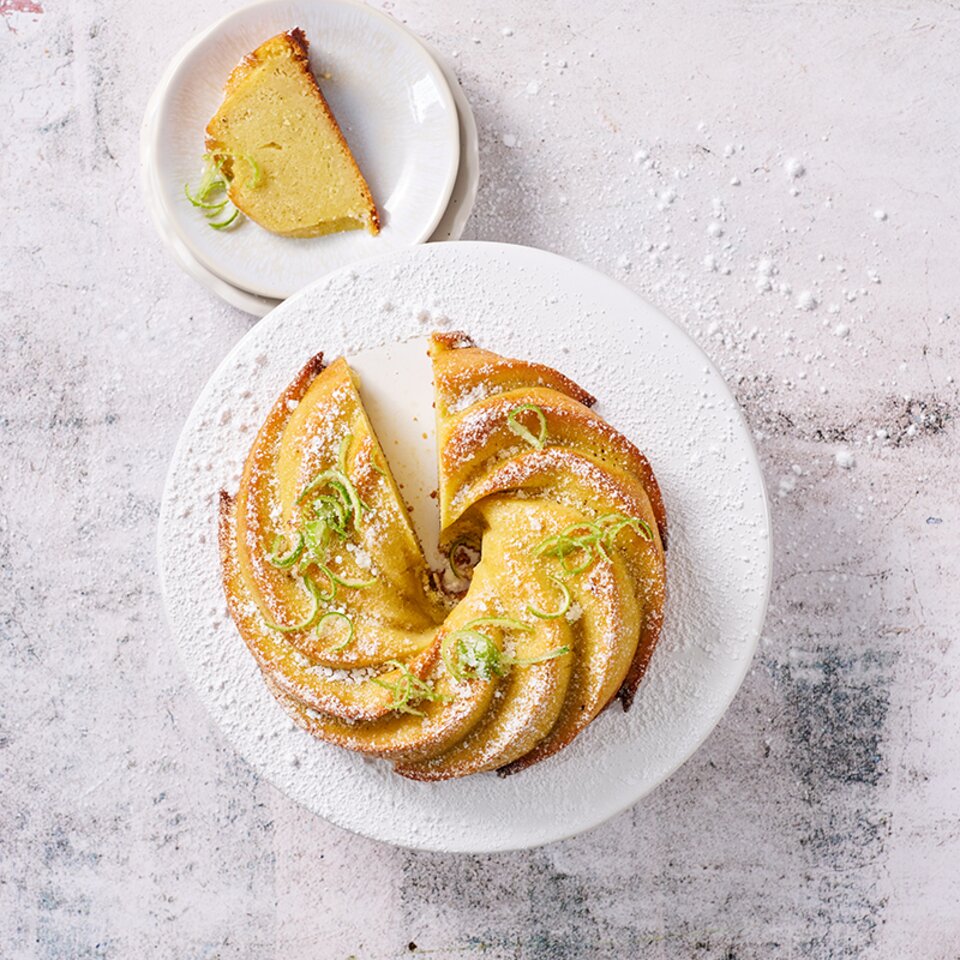 Pikanter Limettenkuchen mit Puderzucker und frischer Limettenschale, serviert mit einer Scheibe auf einem zarten Teller.