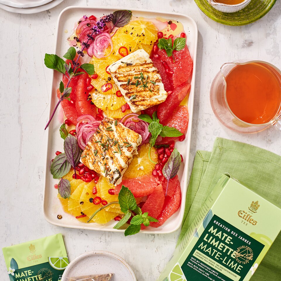Erfrischender Mate-Limettensalat mit Zitrusfrüchten und gegrilltem Halloumi, serviert mit Kräutertee und garniert mit Granatapfel und Minze.
