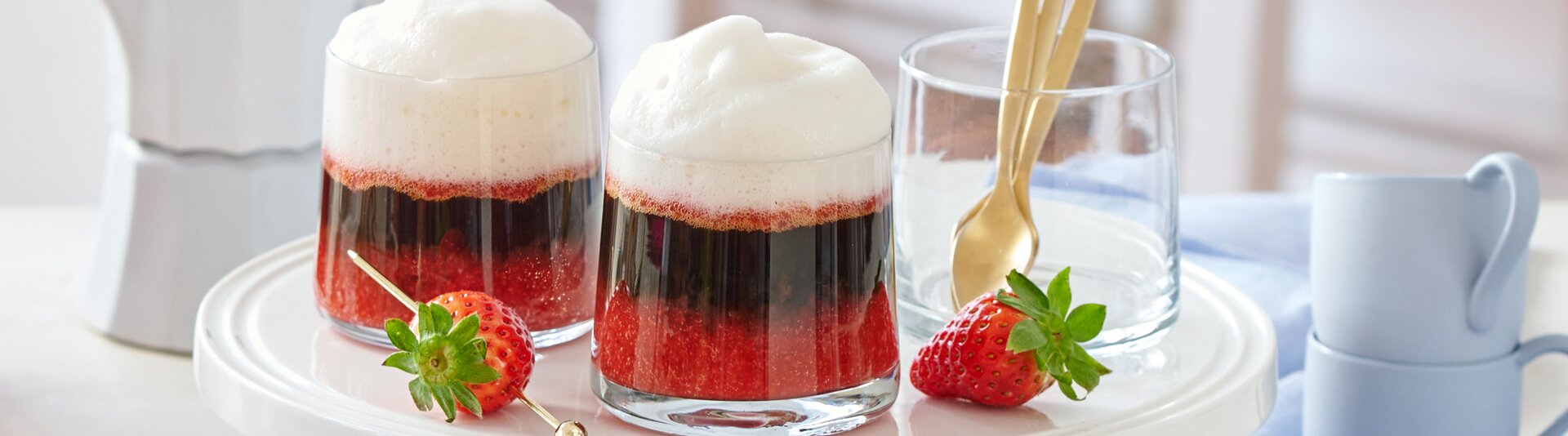 Zwei schön geschichtete Erdbeer-Espresso-Getränke auf einem weißen Tortenständer, verziert mit frischen Erdbeeren und Osterdekor.