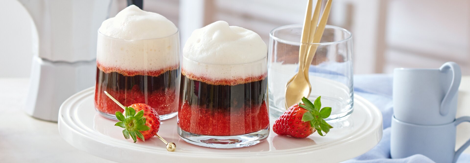 Köstlicher Erdbeer-Espresso, serviert in Glastassen, garniert mit frischen Erdbeeren auf einem stilvollen Kuchenständer.