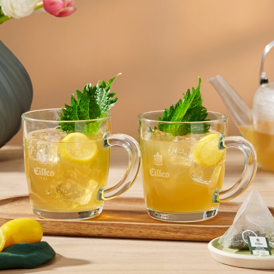 Refreshing green tea with yuzu and ginger beer served in glasses, garnished with lemon and mint on a wooden tray.
