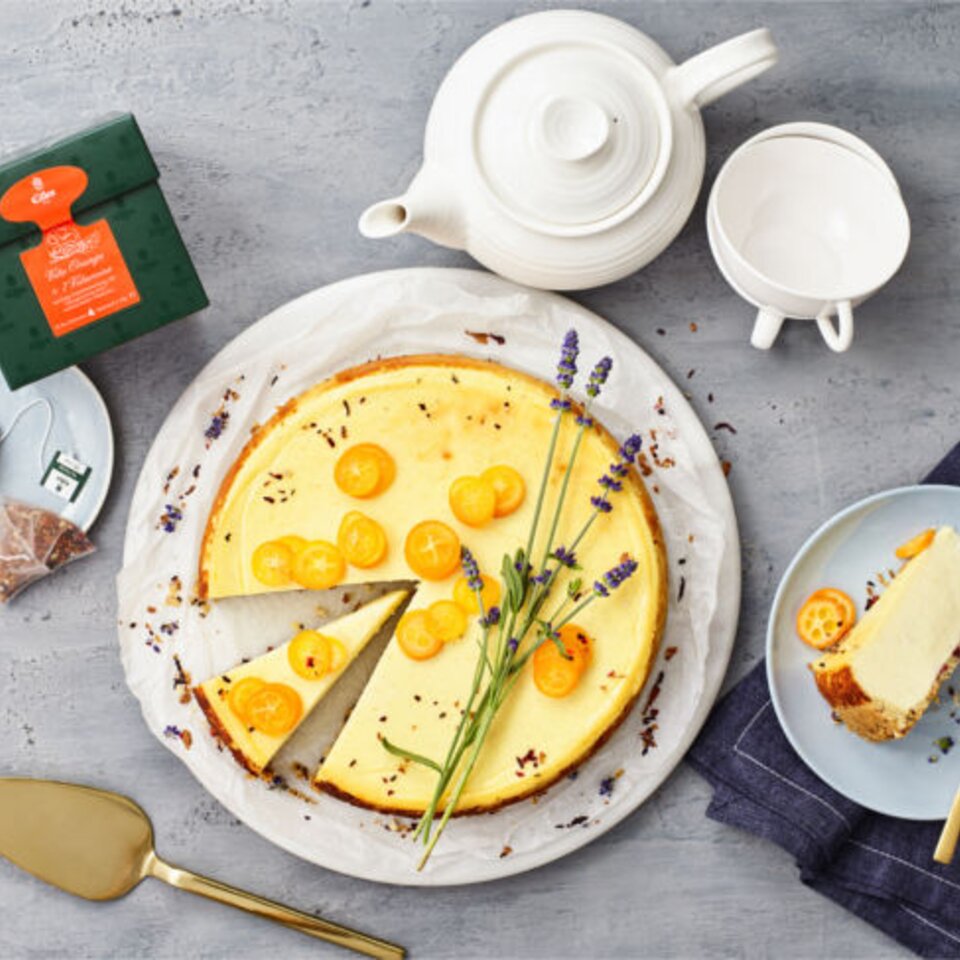 Köstlicher Orangenkäsekuchen mit Lavendel und Kumquats, serviert mit Teezubehör und elegantem Geschirr.