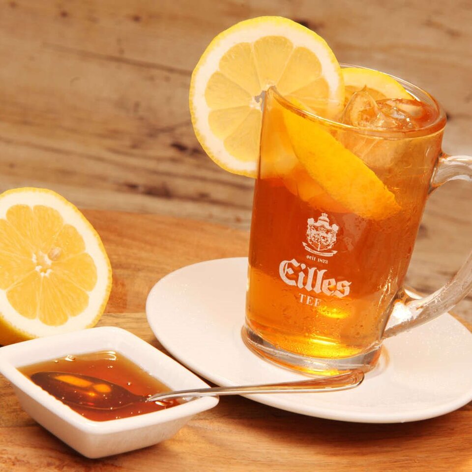 Erfrischender Eistee in einem mit Zitronenscheiben garnierten Glas, serviert mit Honig auf einem Holztisch. Das perfekte Sommergetränk.