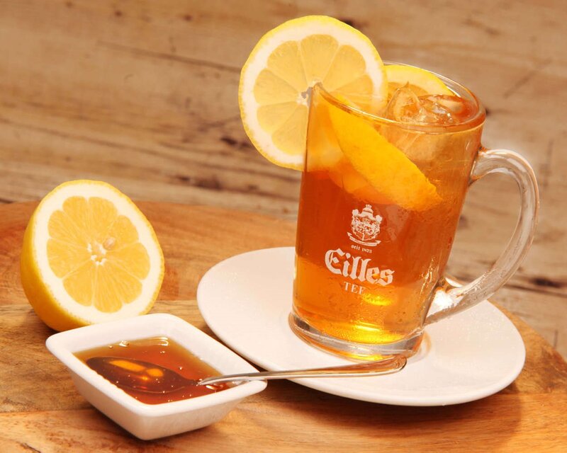 Erfrischender Eistee in einem mit Zitronenscheiben garnierten Glas, serviert mit Honig auf einem Holztisch. Das perfekte Sommergetränk.