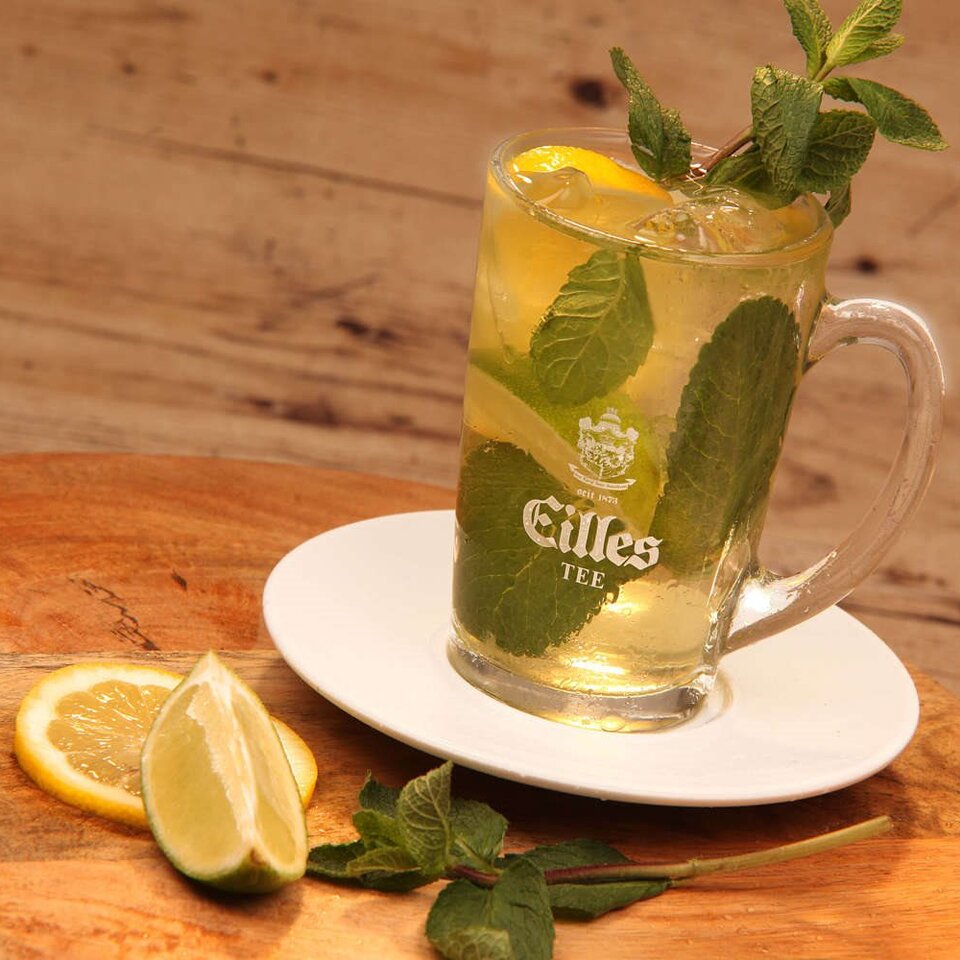 Erfrischender Eistee, garniert mit Zitrone und Minze, serviert in einem Glasbecher auf einem Holztablett.