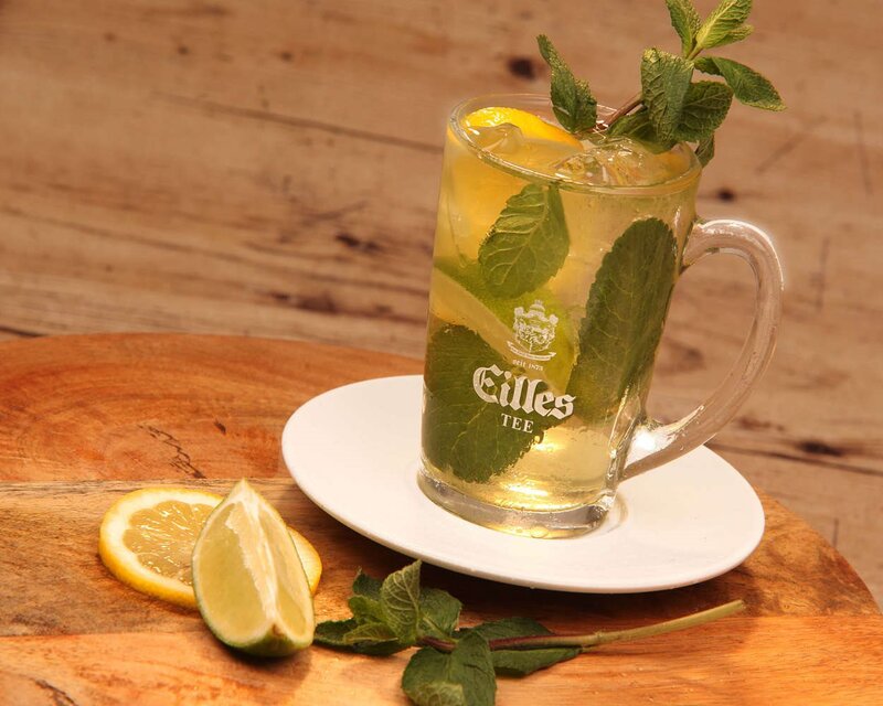 Erfrischender Eistee, garniert mit Zitrone und Minze, serviert in einem Glasbecher auf einem Holztablett.