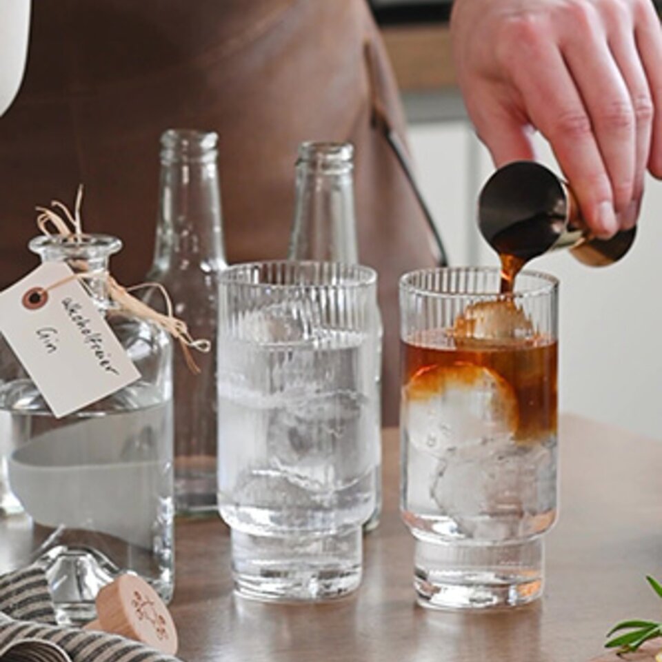 Gießen von mit Kaffee versetztem Gin in ein Glas auf Eis, um eine erfrischende Cocktailkreation zu präsentieren.