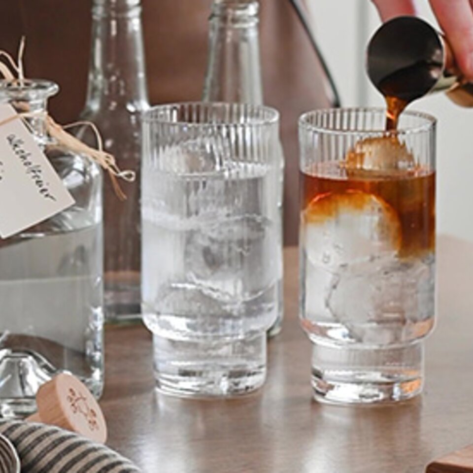 Gießen von mit Kaffee versetztem Gin in ein Glas auf Eis, um eine erfrischende Cocktailkreation zu präsentieren.