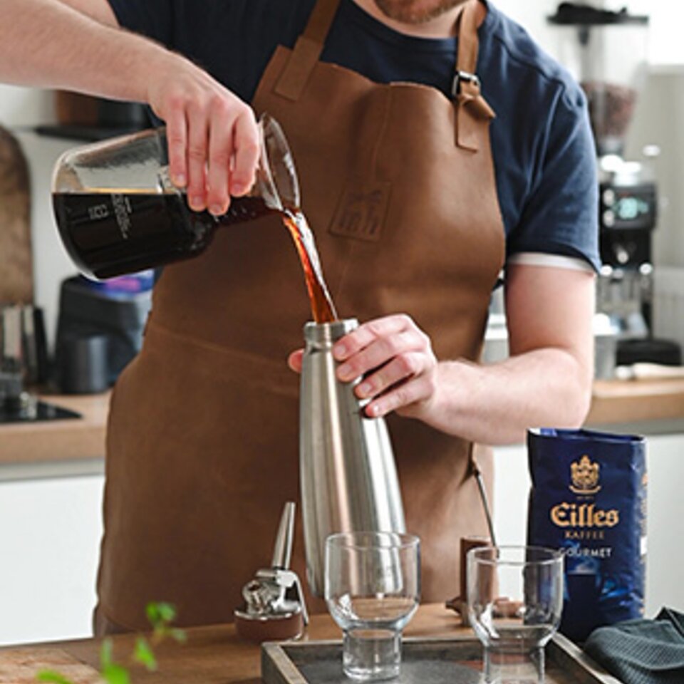 Ein Barista bereitet Nitro-Kaltbrühkaffee zu und gießt ihn aus einem Shaker in Gläser, wobei er eine moderne Kaffeeeinrichtung präsentiert.