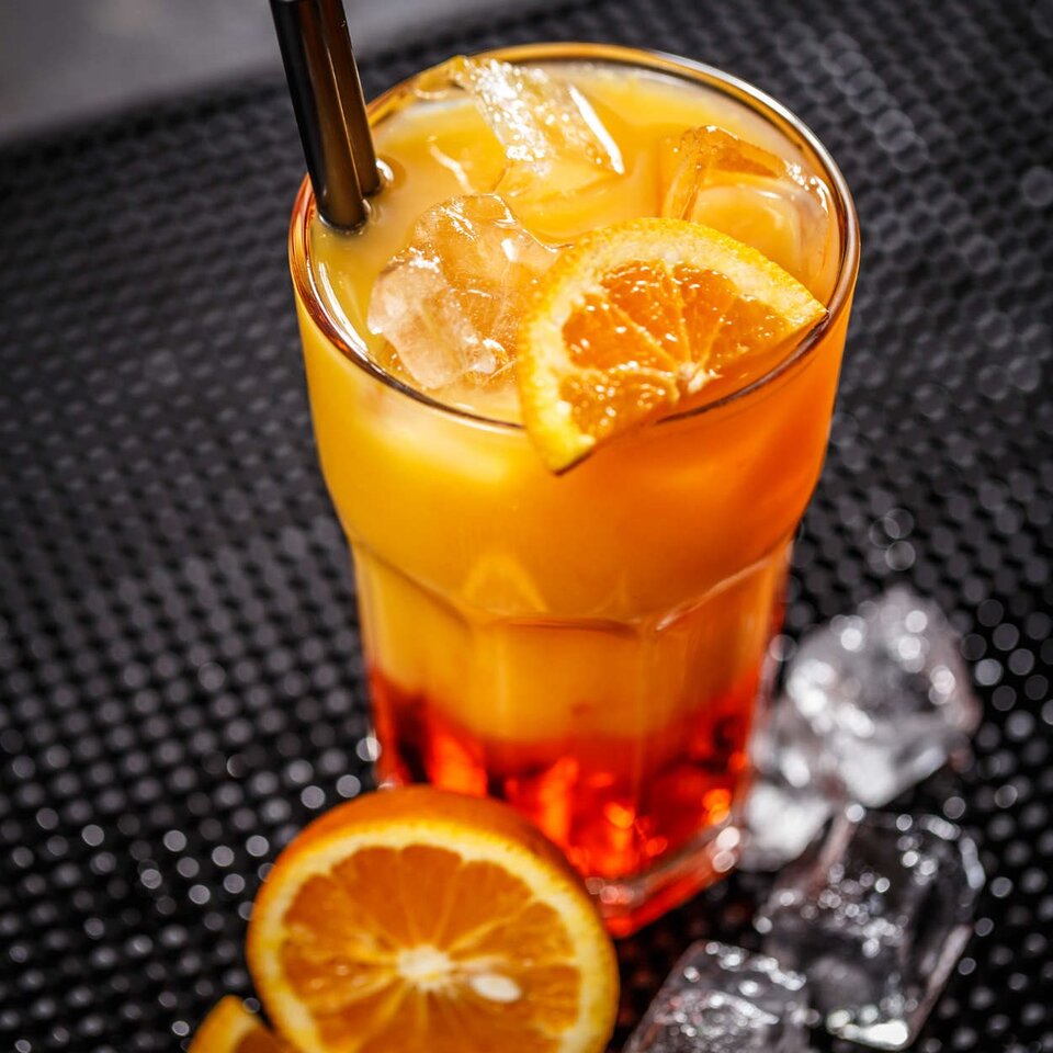 Leuchtend orangefarbener Vita-Cocktail auf Eis serviert, garniert mit einer frischen Orangenscheibe und umgeben von Eiswürfeln.