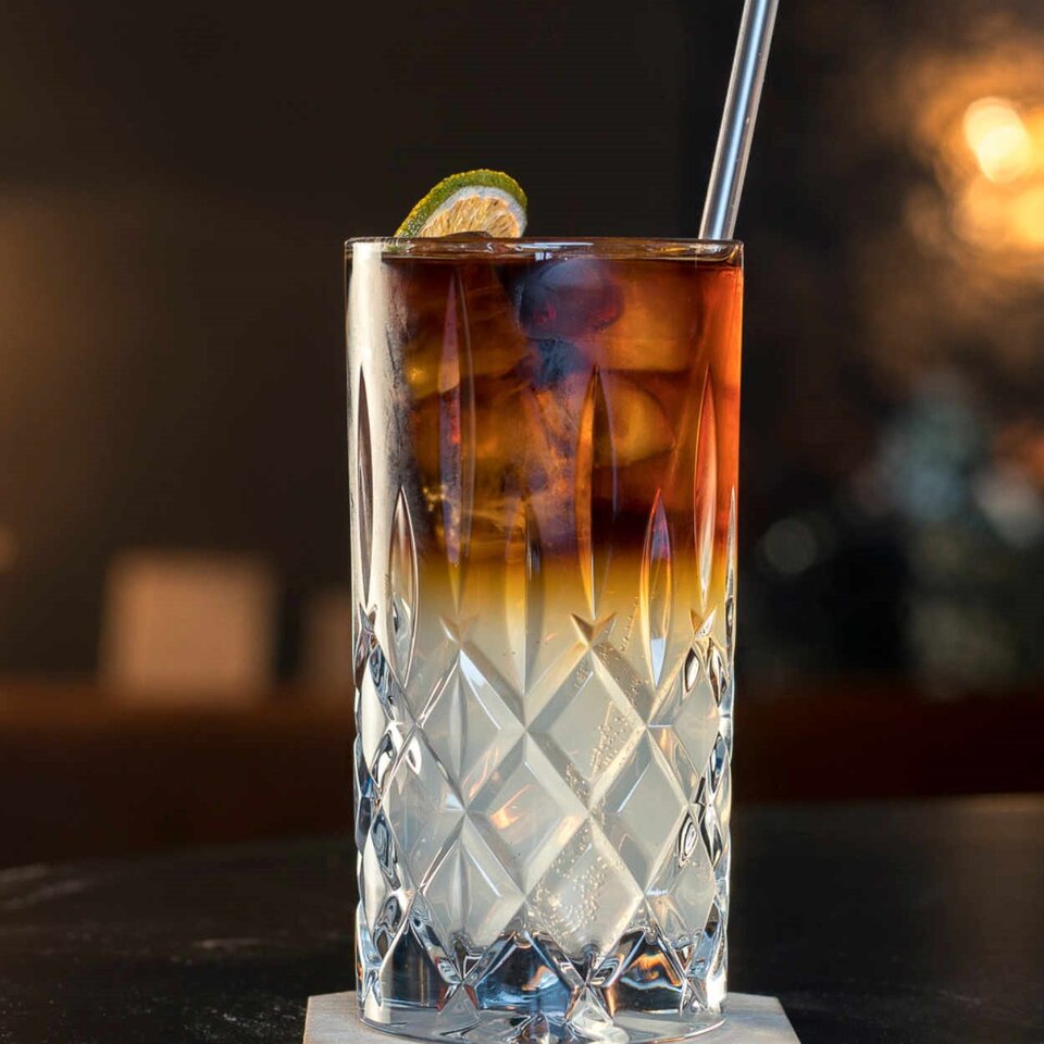 Schickes Kristallglas, gefüllt mit einem Stormy Lemonade-Cocktail mit dunklen und hellen Farbtönen, garniert mit Limette.