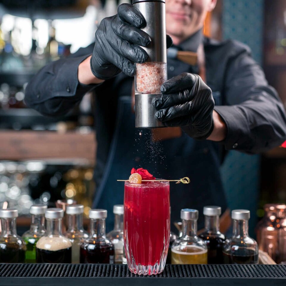 Geschickter Barkeeper bei der Zubereitung eines leuchtenden roten Tee-Cocktails mit Rosenblättern in einer stilvollen Londoner Bar.