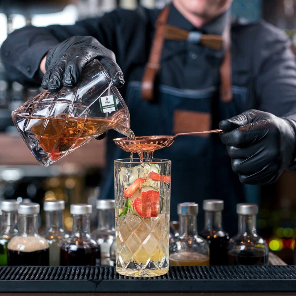 Der Barkeeper gießt einen erfrischenden Zitronen- und Früchtetee-Cocktail in ein Glas, der durch seine lebendigen Zutaten und die elegante Präsentation besticht.