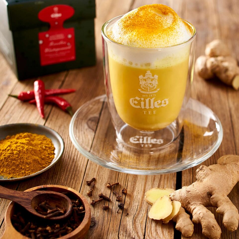 Goldener Winterpunsch mit Gewürzen, Tee und Ingwer, schön präsentiert auf einem Holztisch. Perfekt für ein gemütliches Beisammensein.